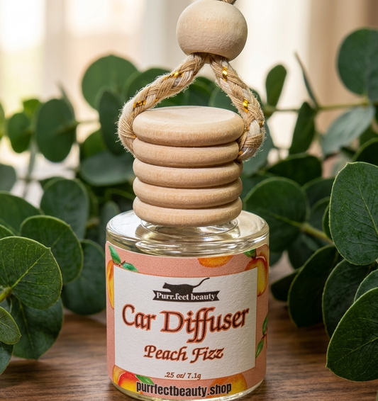 Peach Fizz Car diffuser with wooden design on a wooden surface with green leaves in the background