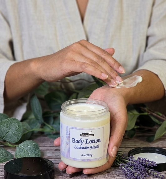Person applying body lotion from a jar labeled 'Lavender Fields' with a wooden background and lavender flowers.
