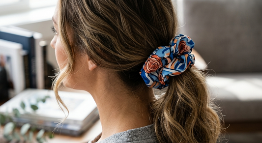 Woman with a colorful scrunchie in her hair, sitting in a room with books and a plant.