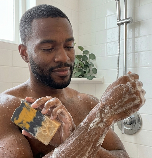 Man in a bathroom applying soap to his arm with a bar of soap.