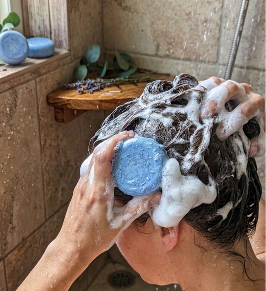 Person washing hair with a blue shampoo bar in a bathroom setting