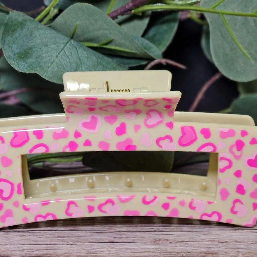 Pink heart print hair clip on a wooden surface with green leaves in the background