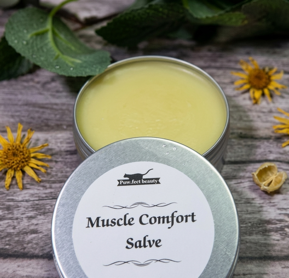 Two tins of 'Muscle Comfort Salve' on a wooden surface with yellow flowers and green leaves.
