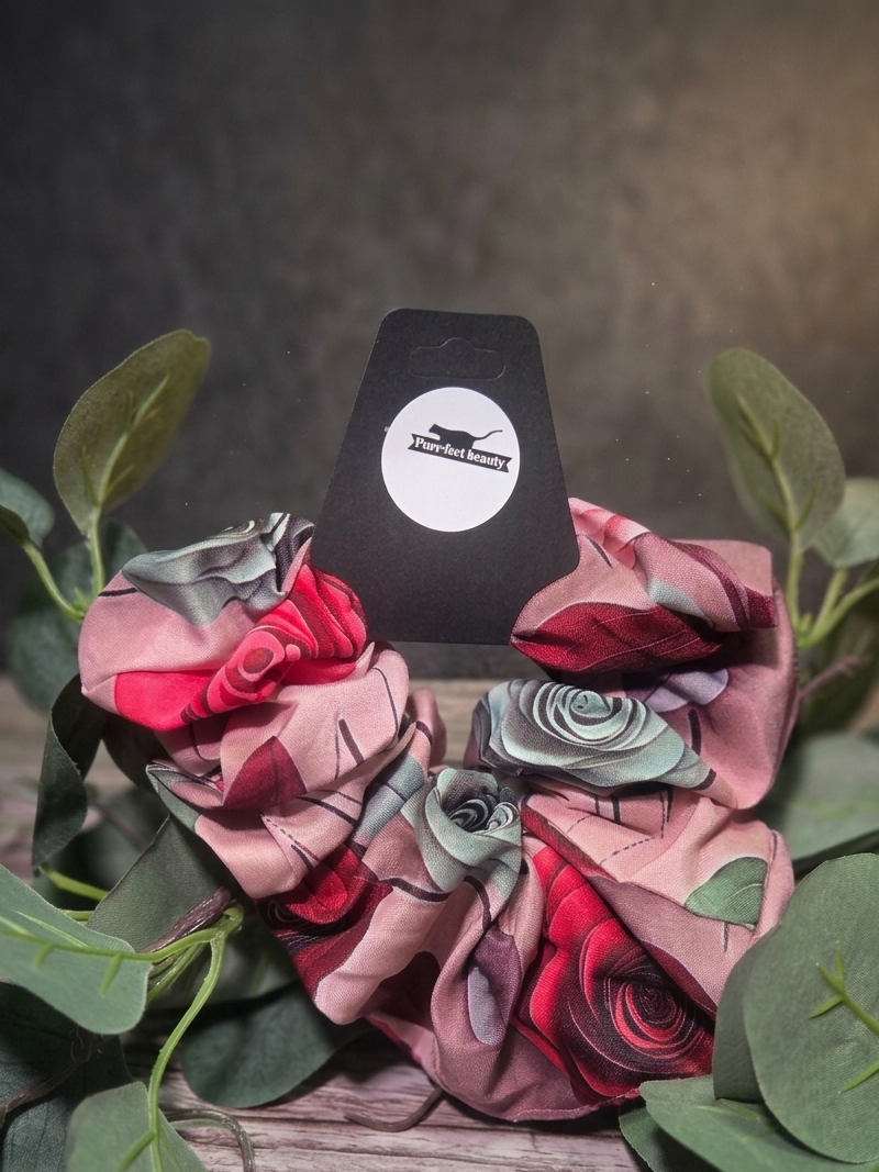 Floral scrunchie with a branded card on a wooden surface with green leaves.