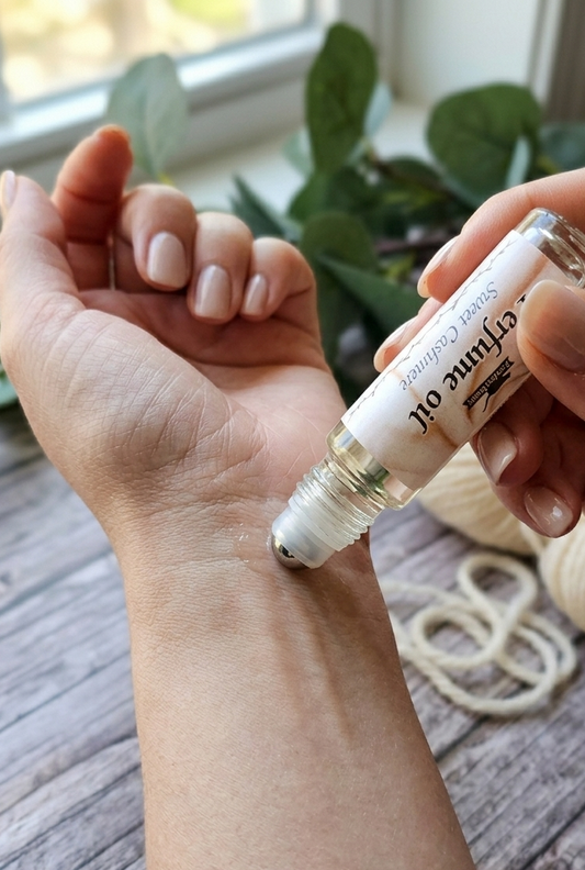 Hand applying a small bottle Sweet Cashmere perfume oil to a wrist with a blurred background