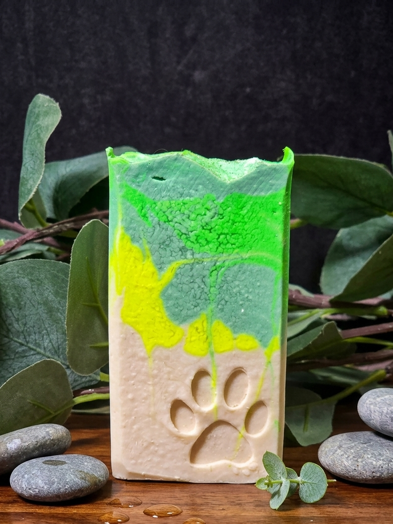 Handmade Lemongrass and Lime soap bar with green and white design, surrounded by eucalyptus leaves and stones on a dark background