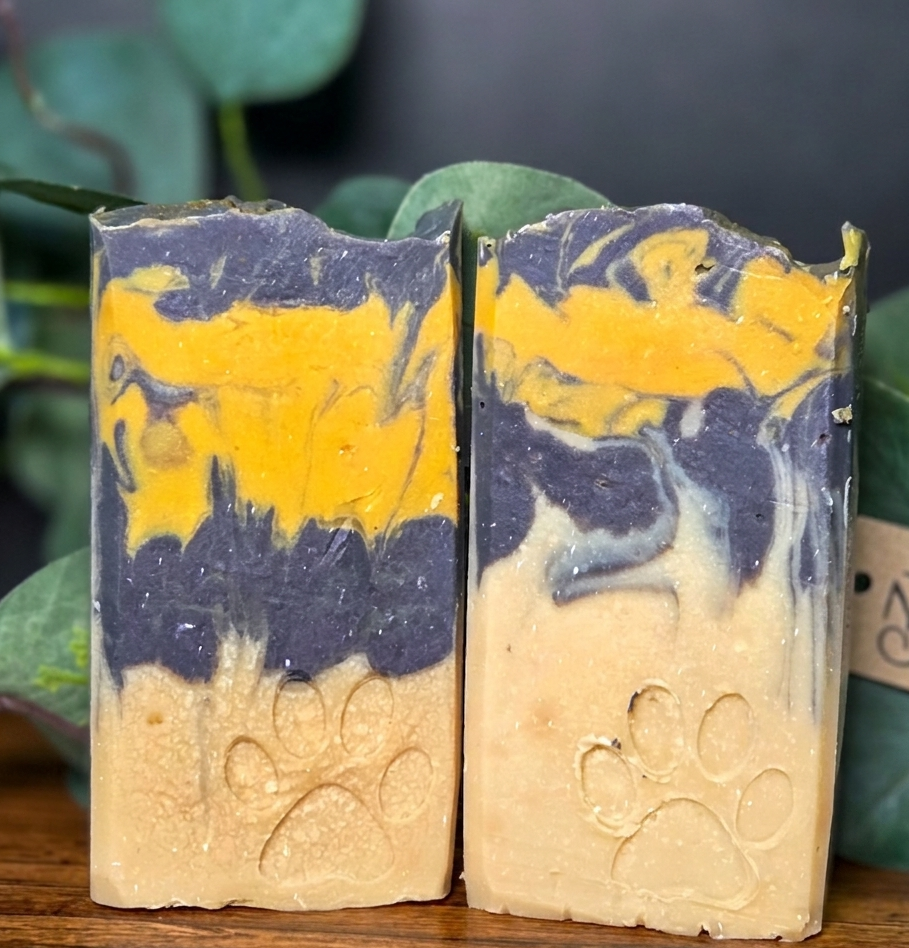 Two bars of Spiced Tea soap with a marbled design of yellow and blue on a wooden surface with green leaves in the background.