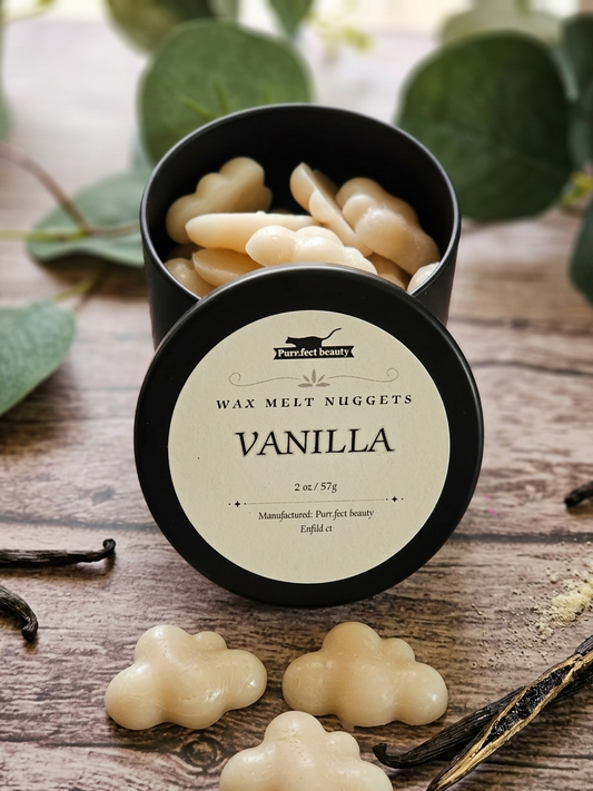 Vanilla wax melt nuggets in a black container on a wooden surface with vanilla beans and leaves.