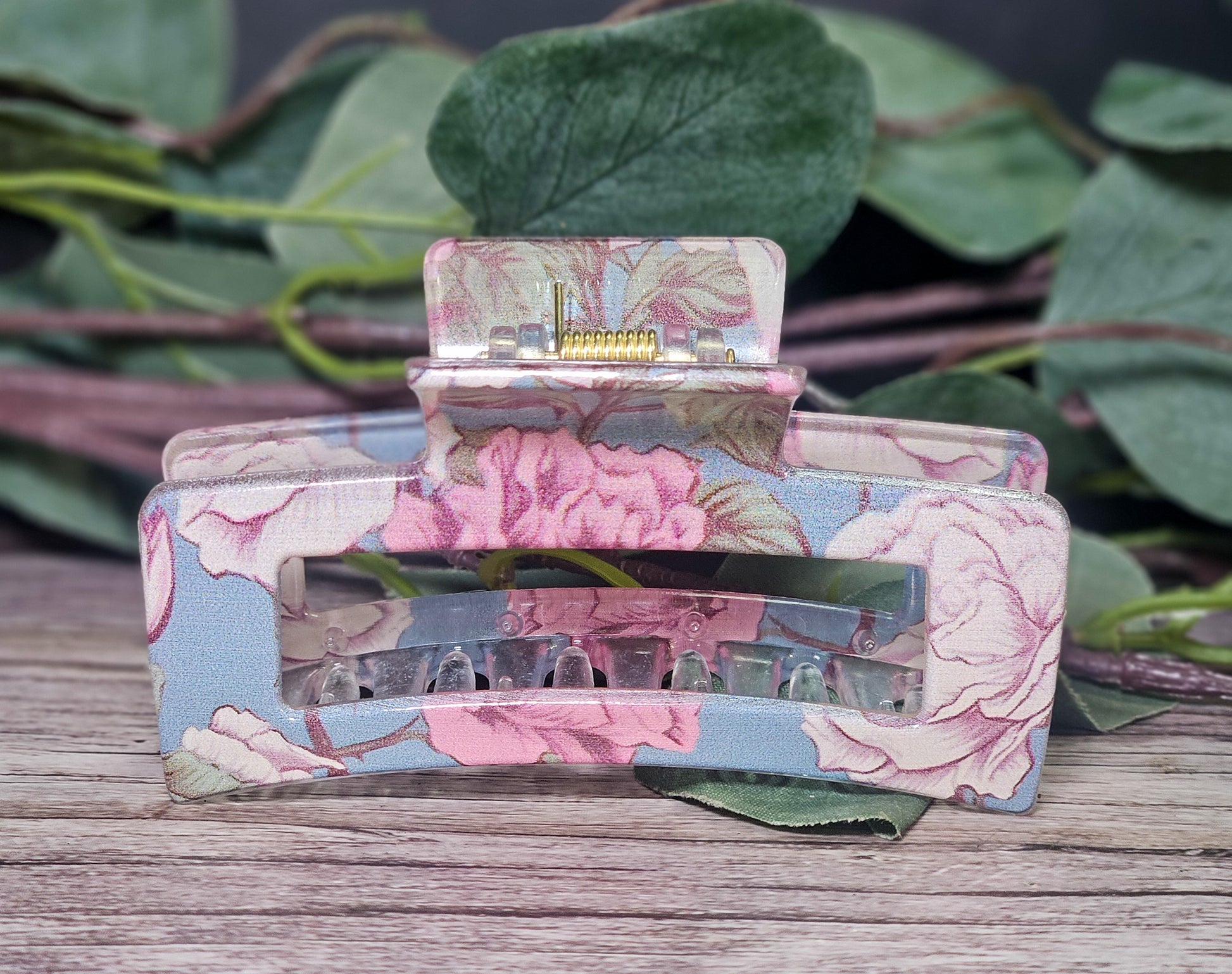 Floral-patterned hair clip on a wooden surface with green leaves in the background