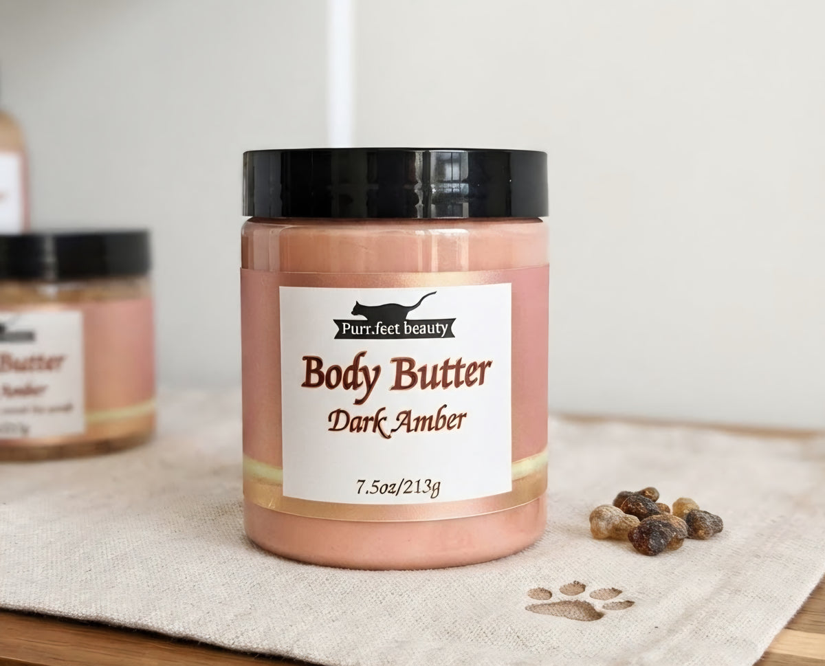 A jar of Purf. Feet Beauty Body Butter in the Dark Amber scent, filled with a dusty dark amber-brown substance and topped with a black lid, resting on a beige linen cloth with small dried botanicals nearby.
