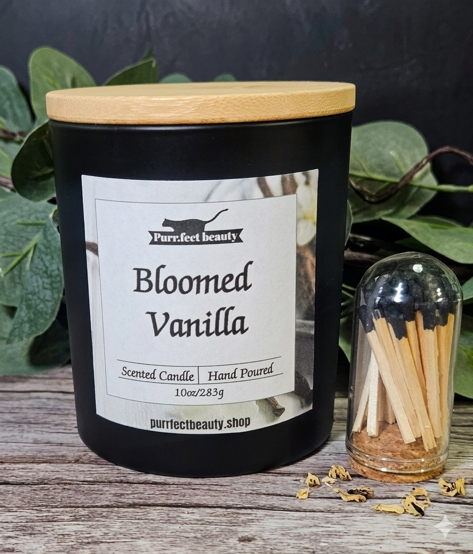 Candle labeled 'Bloomed Vanilla' with a wooden lid and matches on a wooden surface.
