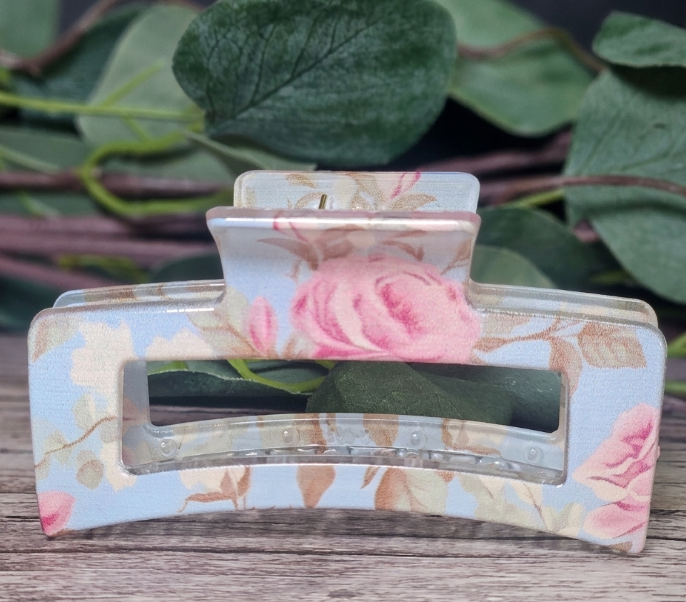 Floral-patterned hair clip on a wooden surface with green leaves in the background