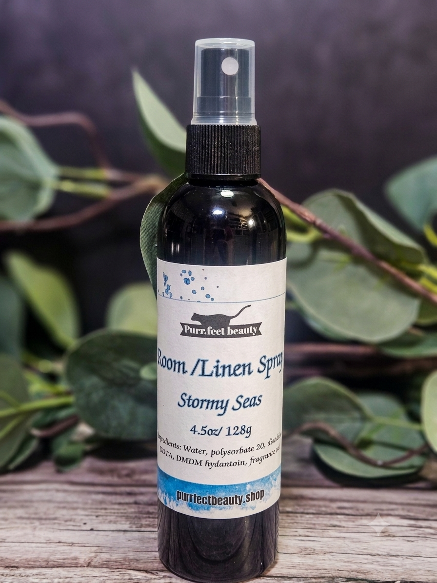Bottle of 'Stormy Seas' room/linen spray with a label on a wooden surface and leafy background