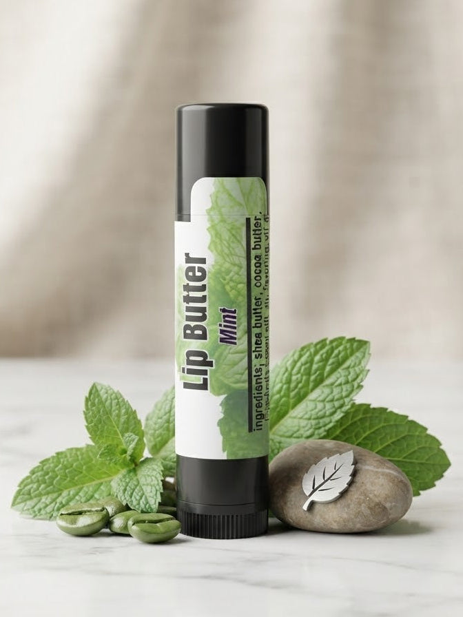 A tube of Lip Butter Mint with a black cap and a white label featuring green mint leaves, styled on a marble surface with fresh mint leaves, coffee beans, and a small stone.
