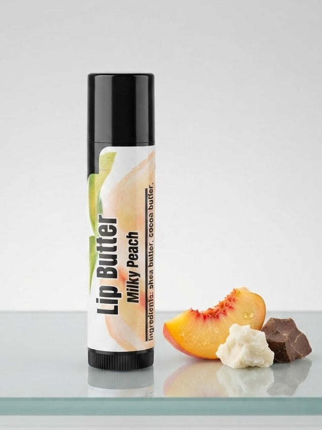 A tube of lip butter labeled 'Milky Peach' stands on a reflective surface next to peach slices, whipped cream, and a chocolate piece against a light gray background.