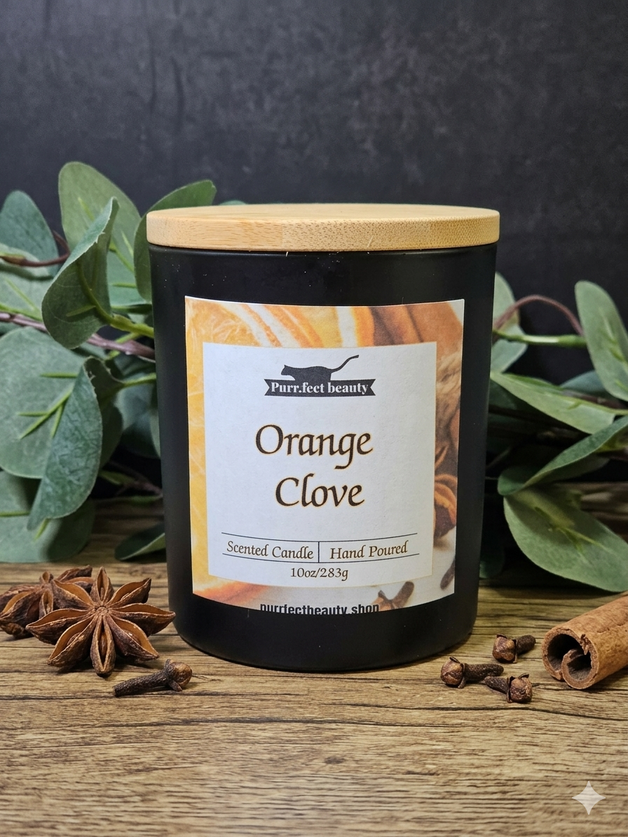 Scented candle labeled 'Orange Clove' with a wooden lid on a wooden surface with greenery and spices.