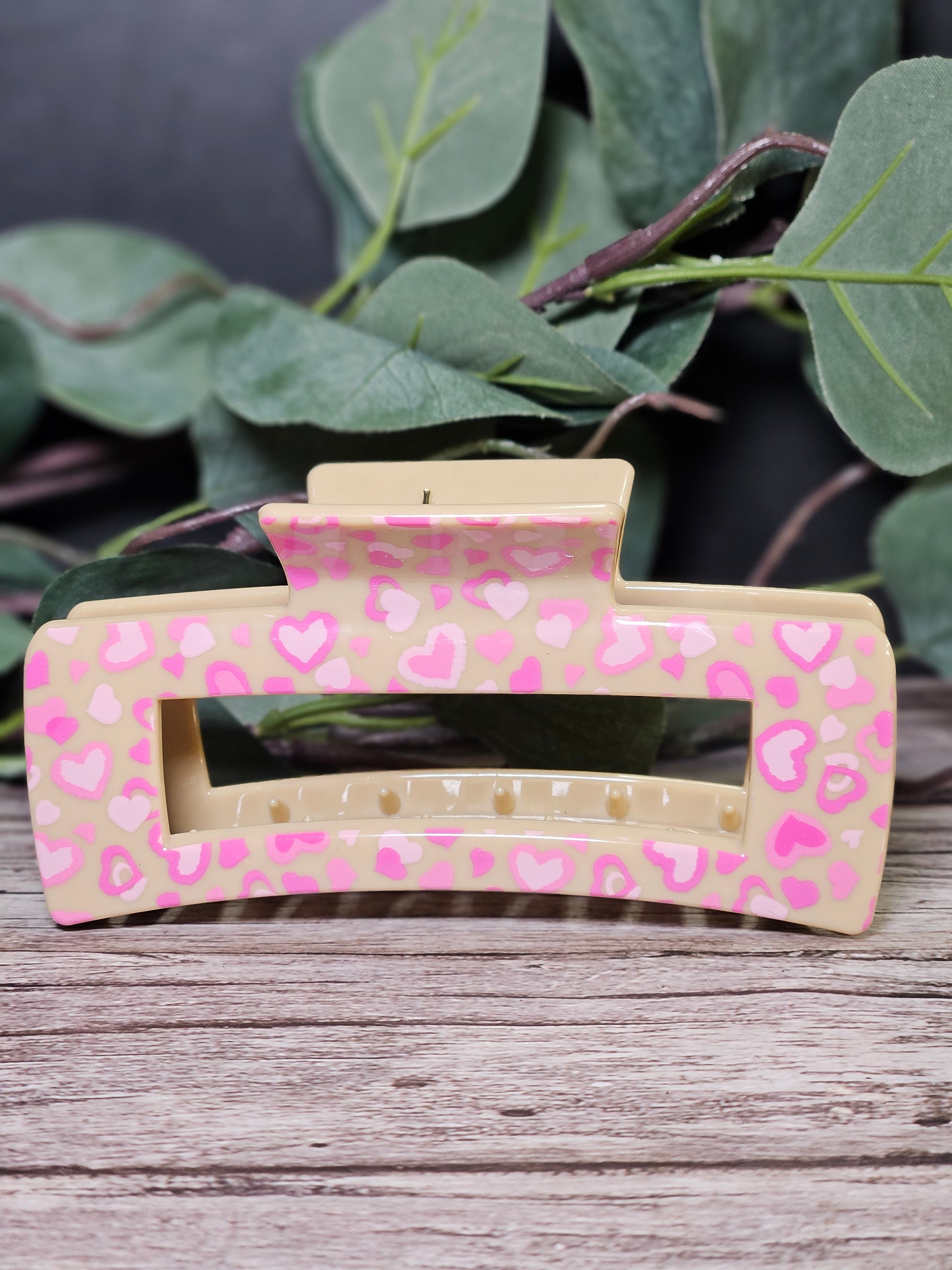 Hair Clip with pink heart pattern on a wooden surface with green leaves in the background