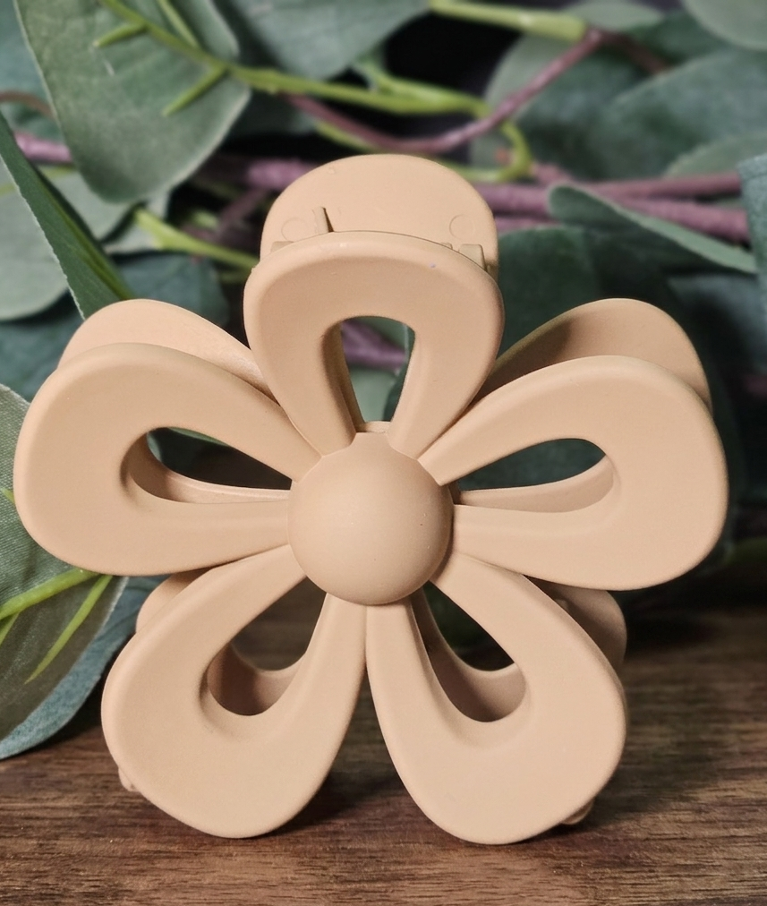 Beige flower-shaped hair clip on a wooden surface with green leaves in the background