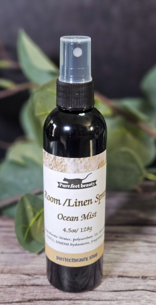 Bottle of Room & Linen Spray labeled 'Ocean Mist' on a wooden surface with greenery in the background.