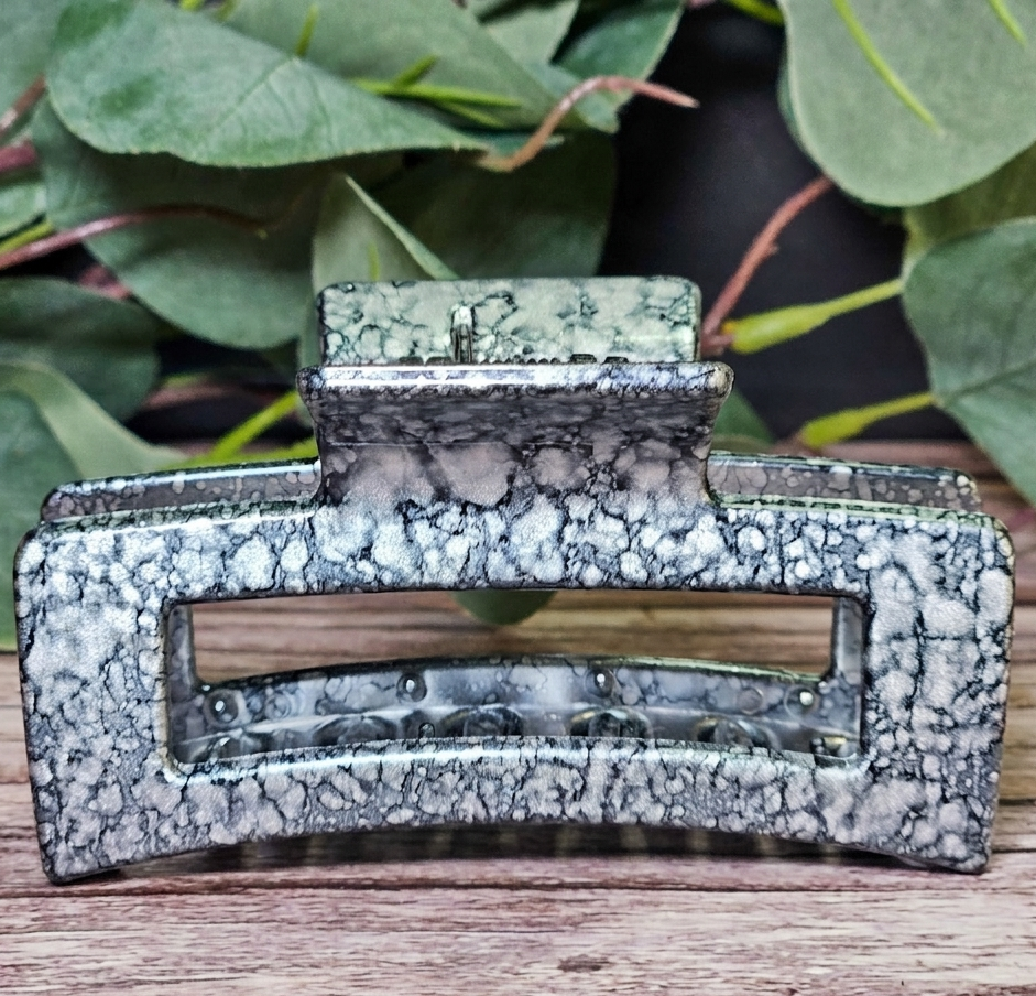 Decorative black speckled claw clip on a wooden surface with green leaves in the background