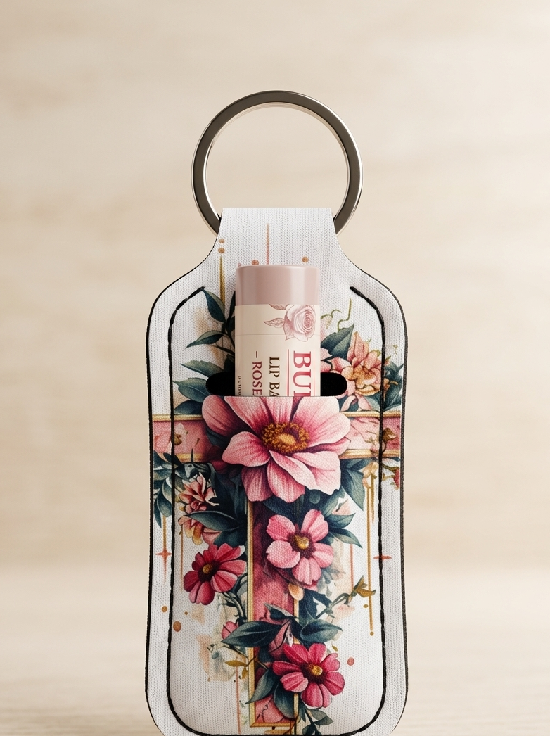 A floral lip balm case with a metal key ring, holding a pink lip balm tube. The case features a white background decorated with pink and red flowers, green leaves, and gold vertical stripes, set against a light wood background.