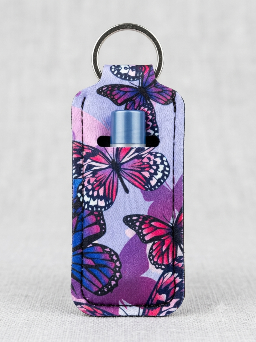 A small rectangular keychain case with a butterfly print in pink, purple, and blue, featuring a silver metal key ring at the top and a small blue cylindrical insert visible in the center.