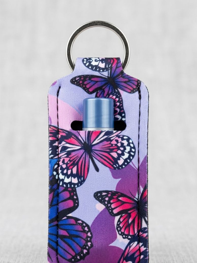 A small rectangular keychain case with a butterfly print in pink, purple, and blue, featuring a silver metal key ring at the top and a small blue cylindrical insert visible in the center.