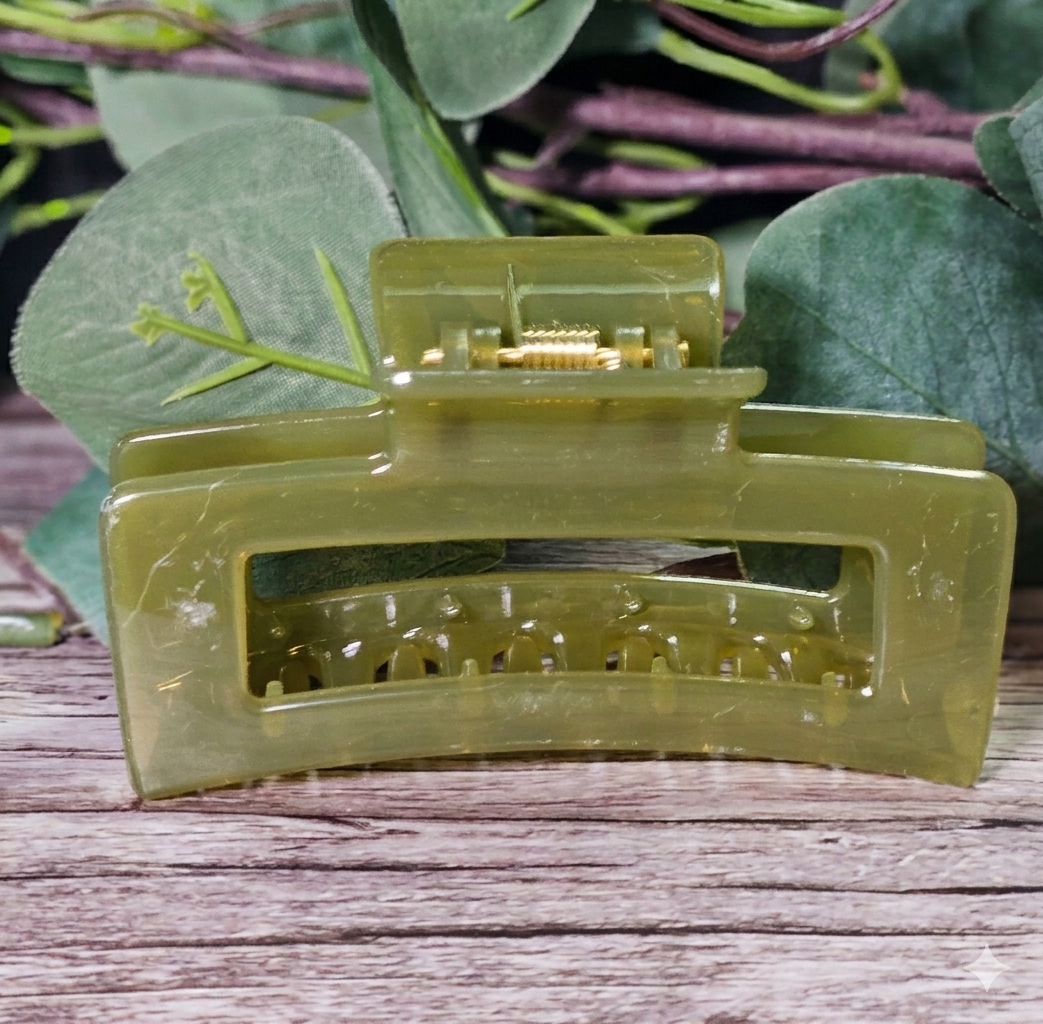 Green hair clip on a wooden surface with green leaves in the background