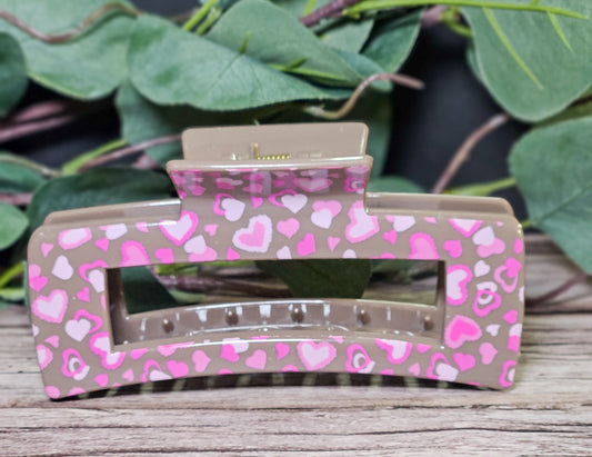 Hair Clip with pink heart pattern on a wooden surface with green leaves in the background