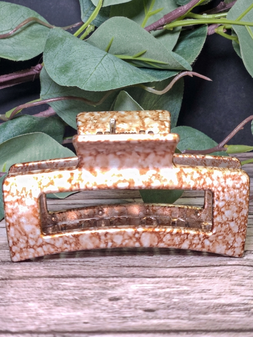 Decorative hair clip with a speckled pattern on a wooden surface with green leaves in the background