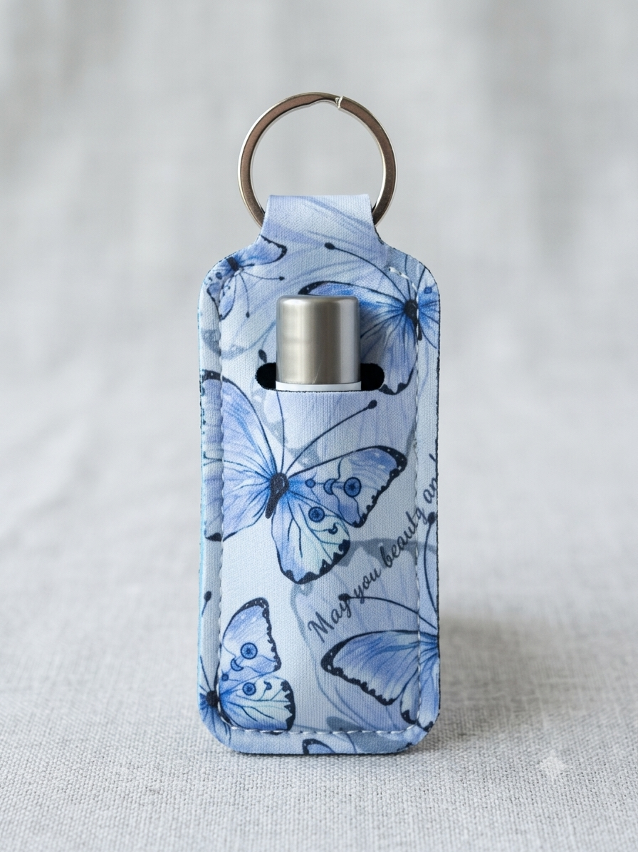 A small insulated bottle holder or keychain pouch with a butterfly print in shades of blue and white, featuring a silver metal bottle insert and a gold-toned key ring, set against a light gray textured fabric background.