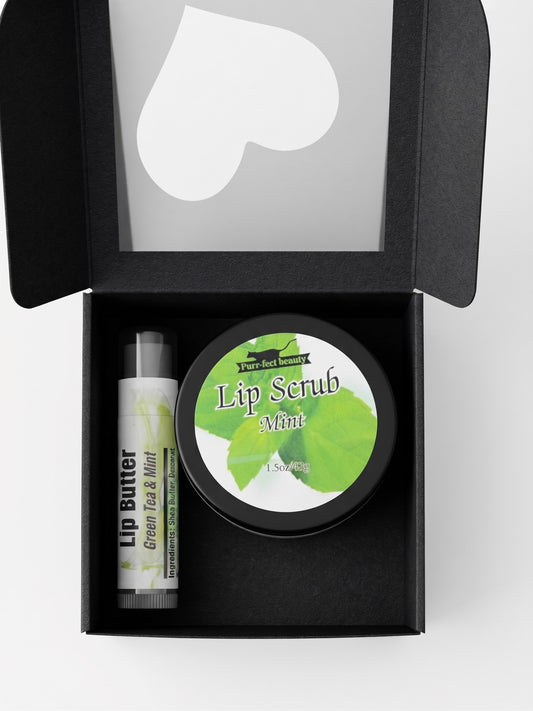 A black gift box containing a tube of lip butter and a round tin of lip scrub, both labeled Green Tea & Mint, shown on a light gray background.
